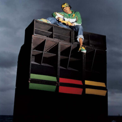 Back of a man at a concert. Hes wearing a beanie hat and a baggy denim jacket with studs. Photo with a purple hue